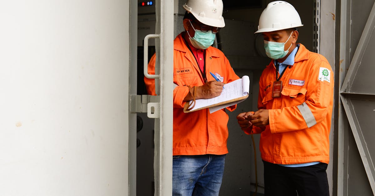 Two construction workers in safety gear discussing plans at a site entrance.