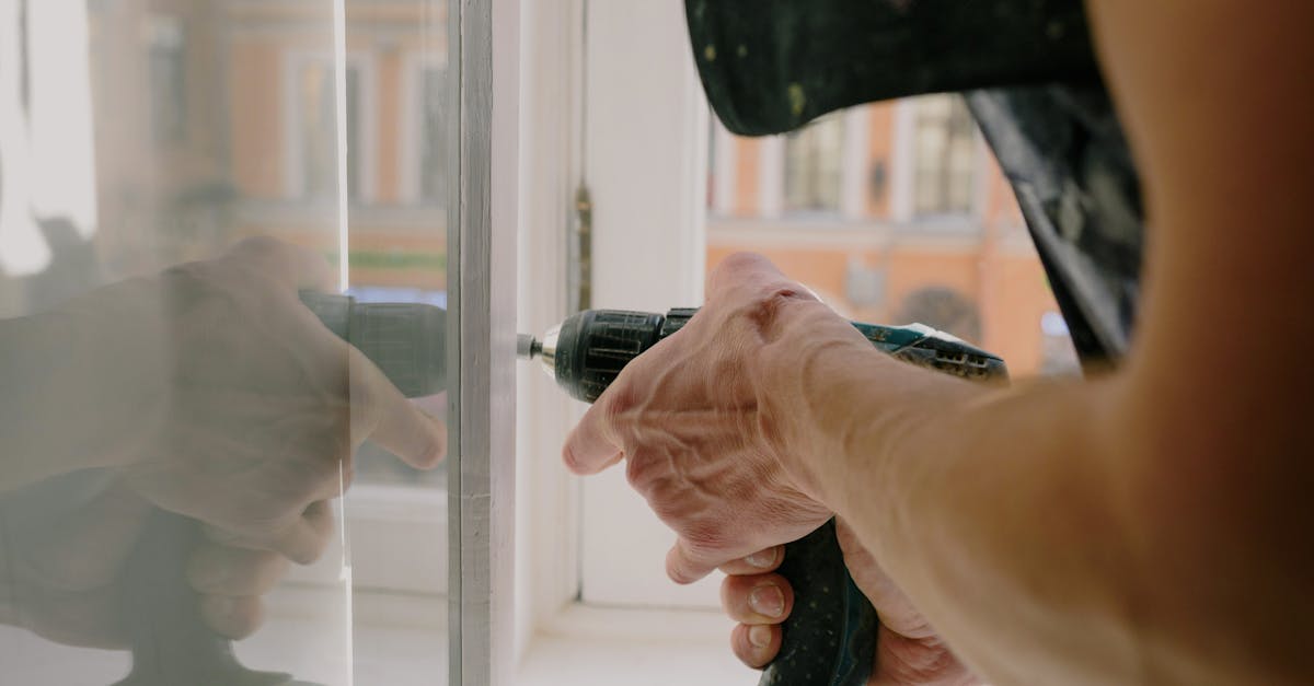 Close-up of a handyman's hands using a drill to fix a window inside an apartment.