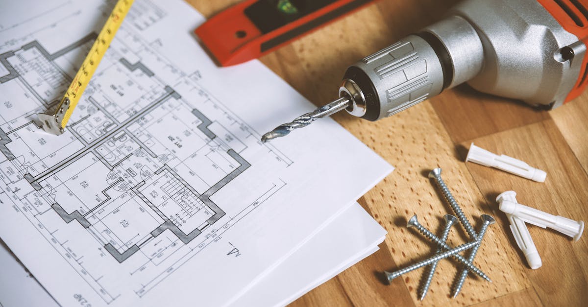 Close-up of construction blueprint with tools like drill and screws on a wooden table.