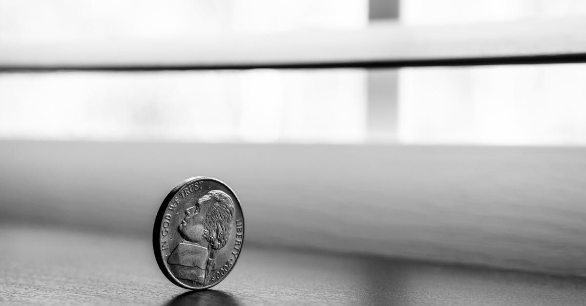 Monochrome close-up of a standing coin reflecting on a smooth surface.